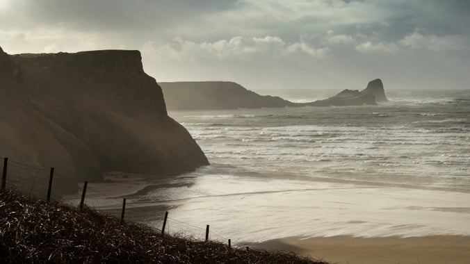 A beach with rocks sticking up out of the sea and waves crashing on it in evening light